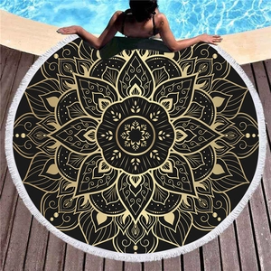 Thick black and gold mandala round beach towel with white tassels on a poolside wooden deck