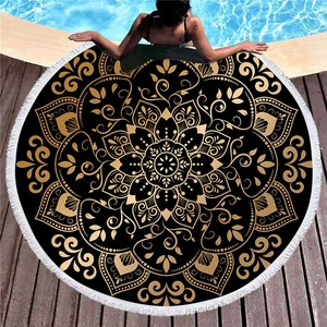 Thick black and gold mandala round beach towel with white tassels on a poolside deck