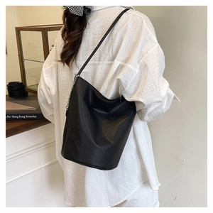 Fashionable black pebbled tote bag shown on a model with chain and leather straps