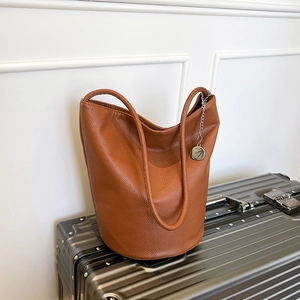 Minimalist brown pebbled leather bucket bag with silver chain on a silver suitcase