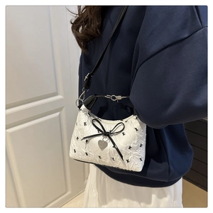 Detail of white mini bucket bag with black embroidery, silk bow, and silver heart charm