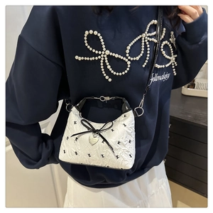 Detail of white textured crossbody bag with black letter print and heart pendant