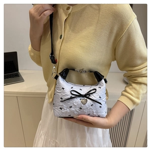 Detail of white embossed fabric handbag with black bow prints and heart pendant