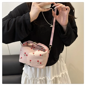 Detail of pink corduroy crossbody bag featuring red cherry prints and golden lock buckle