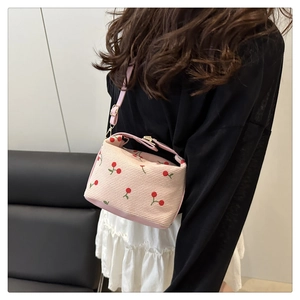 Close-up of pink cherry print corduroy crossbody bag worn by a model in casual setting