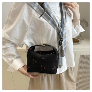 Close-up of black knit shoulder bag with red cherry patterns and snap button detail