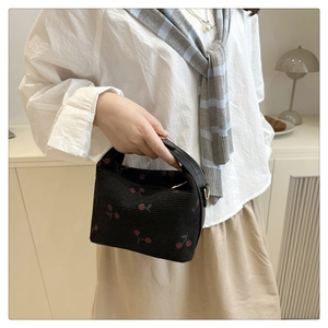 Detail of black corduroy shoulder bag with red cherry print and leather handles