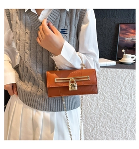 Detail der karamellbraunen Krokodilmuster-Handtasche mit Goldgriff und Kette am Modell
