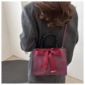 Close-up of burgundy bridal handbag with large satin bow and woven handle on tweed suit