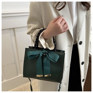 Vue détaillée d'un sac à main vert foncé avec nœud bleu et poignée en cuir tressé
