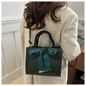 Detail of dark green handbag with large satin bow and woven handle on elegant model