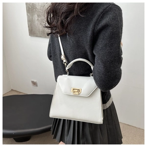 Close-up of white crossbody bag with gold metal twist lock and minimalist handle