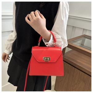 Detail of red leather crossbody bag featuring a rectangle gold clasp and handle