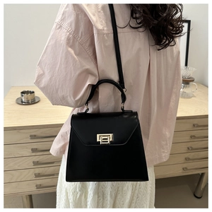 Close-up of elegant black matte leather handbag with gold metal clasp on model