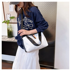 Detail of white nylon messenger bag with black shoulder strap and orange zipper accent
