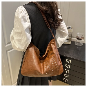 Detail der braunen Vintage-Tasche mit Metallnieten-M-Logo und verstellbarem Schultergurt