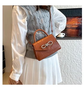 Detail of orange-brown crocodile embossed handbag featuring a sparkling rhinestone bow