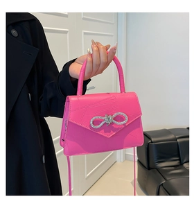 Detail of a bright pink crocodile pattern handbag with a sparkling rhinestone bow buckle