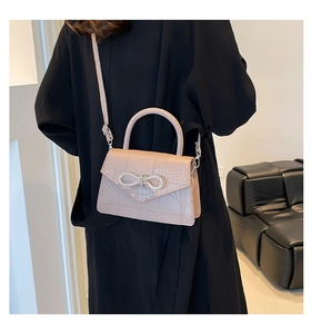 Model wearing a pink crocodile pattern crossbody bag with a sparkling rhinestone bow