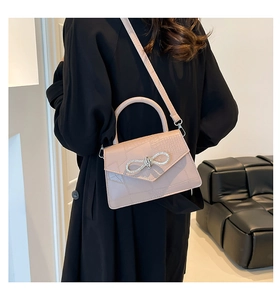 Detail of pink croc-embossed handbag with rhinestone bow on black coat background
