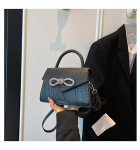Detailed view of black crocodile pattern handbag with a sparkling rhinestone bow buckle