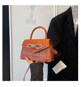 Detail of orange faux-leather handbag with crocodile texture and rhinestone bow buckle