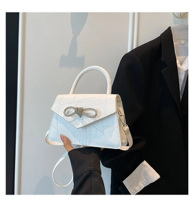 Detail of white faux crocodile leather handbag with a sparkling rhinestone bow buckle