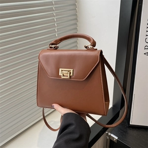 Brown leather crossbody handbag with gold twist lock and single handle in urban setting