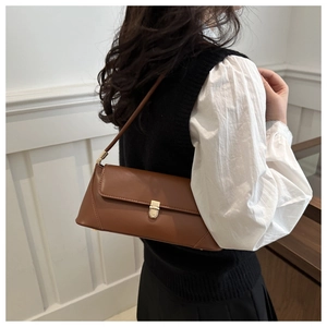 Detail of dark brown baguette shoulder bag with gold metal clasp on a female model