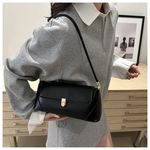 Minimalist black baguette bag shown on shoulder with golden metal clasp and matte leather