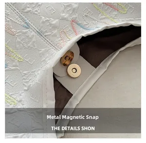 Macro view of gold magnetic snap button and colorful embroidery on white tote bag