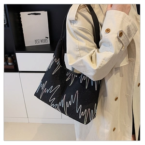 Detail of black tote bag featuring colorful wave embroidery and leather strap on model