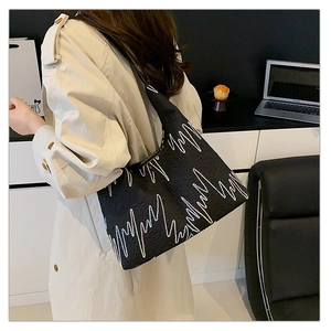 Detail of black hobo bag with wave embroidery worn over a beige trench coat