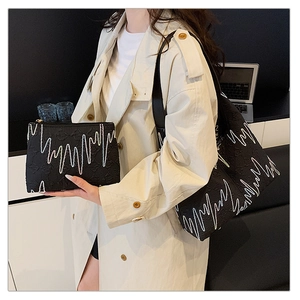 Detail of black tote set with white wavy embroidery and embossed texture on shoulder bag
