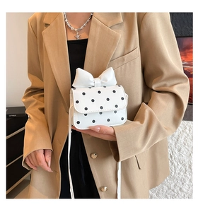 Detail of a mini polka dot crossbody bag with a large bow shown on a khaki blazer