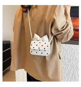 Close-up of mini white crossbody bag with black polka dots and a large bow decoration
