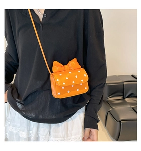 Close-up of bright orange mini polka dot crossbody bag with a large decorative bow