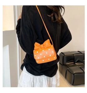 Close-up of bright orange crossbody bag with white polka dots and large bow detail