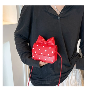 Detail of red polka dot crossbody bag with bow decoration worn on black clothing
