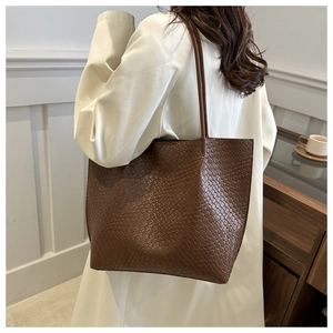 Detail shot of a dark brown woven texture tote bag worn over a beige trench coat