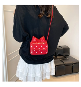Detail view of the red polka dot crossbody bag with a large 3D bow on the back of a child
