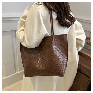 Dettaglio della borsa tote marrone scuro con trama intrecciata indossata su un cappotto