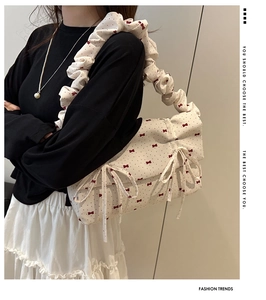 Detail of beige shoulder bag featuring red bow prints and ruffled strap design