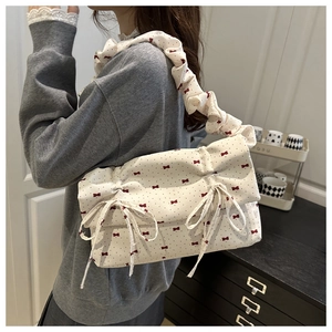 Detail of white ruffled shoulder bag with red bow prints and bow-knot accents on handle