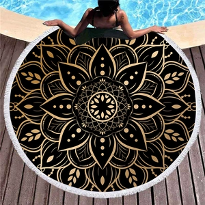 Round black and gold mandala beach towel with white tassels displayed by a pool deck
