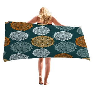 Bohemian beach towel with orange and white mandala patterns on a dark teal background