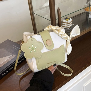Chic cream and green bucket bag with silk handle and floral charm on a wooden table