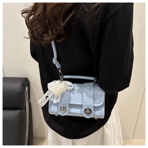 Détail d'un petit sac bleu clair en cuir verni avec double fermoir et nœud de perles dentelle