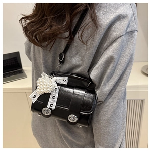 Détail du sac bandoulière en cuir verni noir avec nœud en dentelle et pendentif cœur perlé