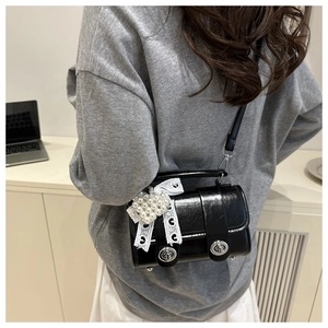 Détail d'un sac à main noir brillant avec nœud en dentelle blanche et perle de cœur